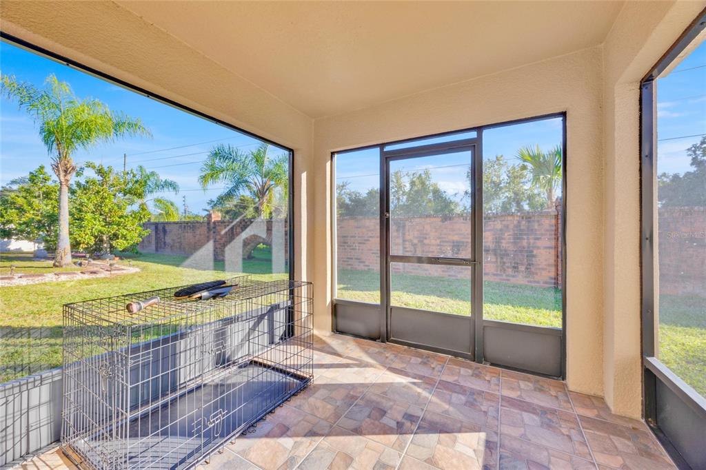 A screened-in porch features tiled flooring, a metal pet crate, and views of a backyard — 4647 CAVERNS DRIVE, KISSIMMEE, FL