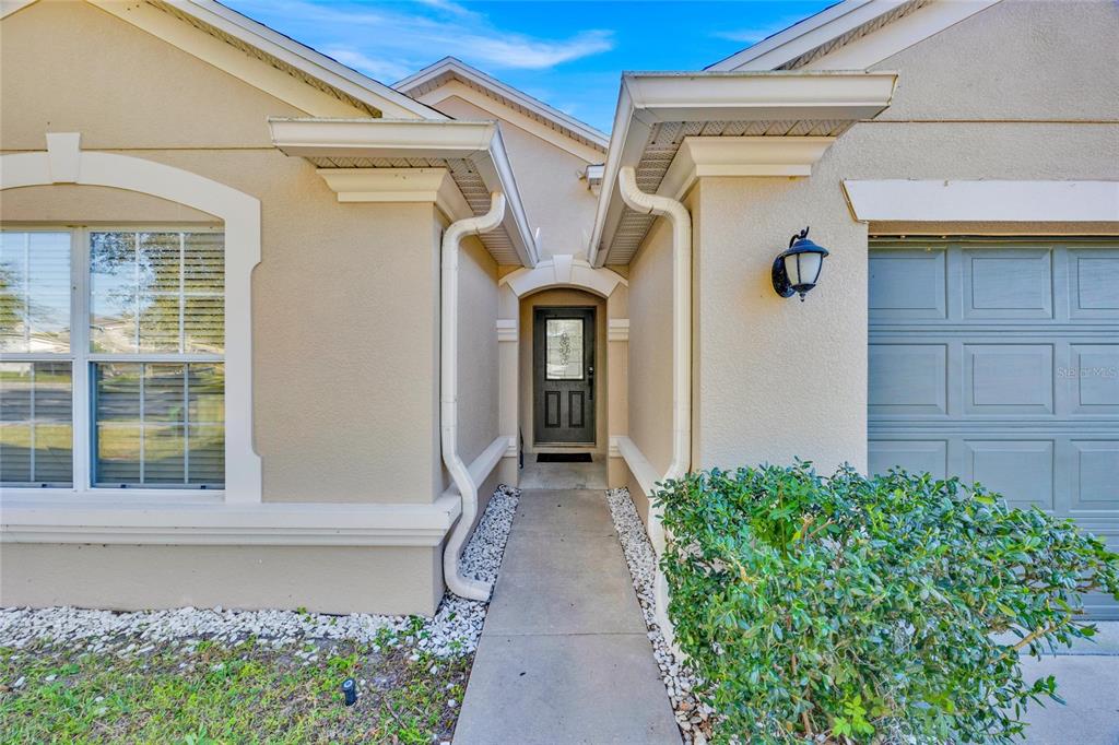 A concrete walkway leads to the front entrance of a beige house with a garage — 4647 CAVERNS DRIVE, KISSIMMEE, FL