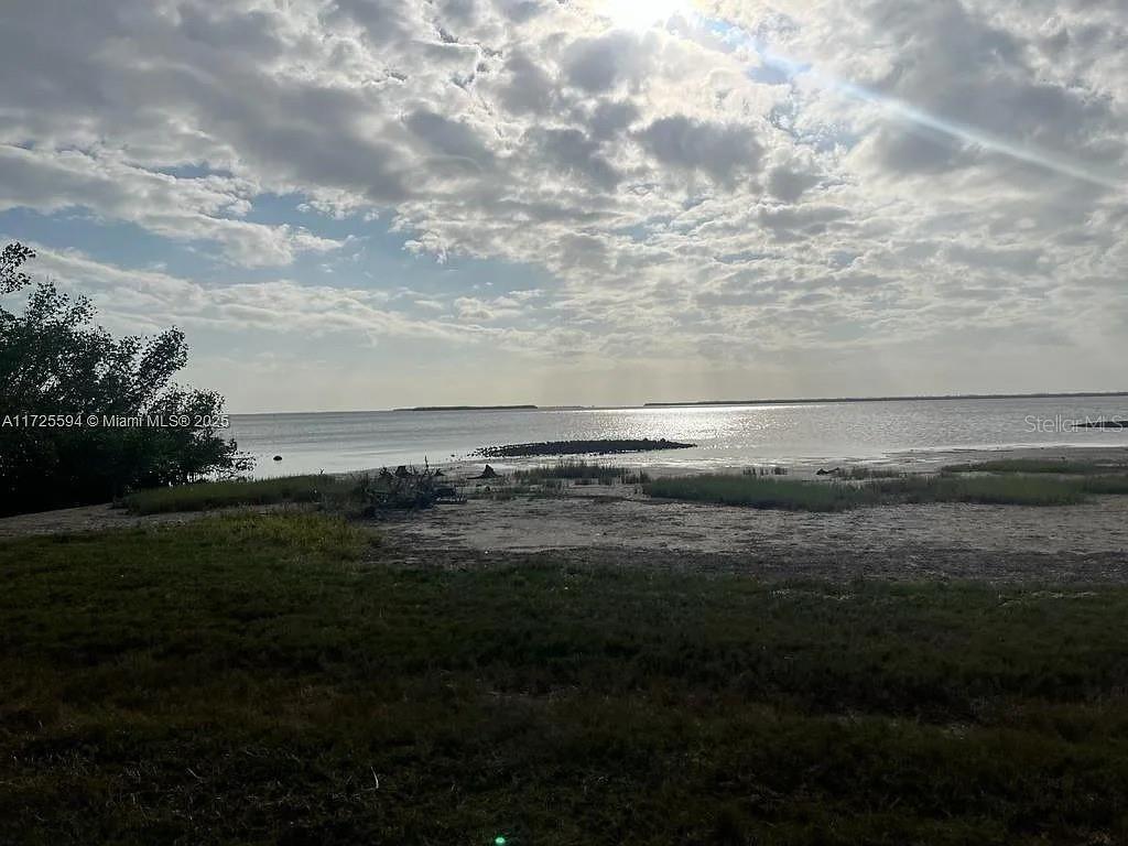 A view of a sandy shoreline, marsh grass, and calm water under a cloudy sky — 7231 SUNDIET BOULEVARD, BOKEELIA, FL