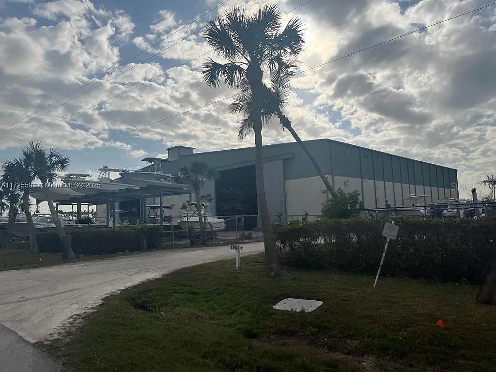 A large industrial warehouse building stands behind a gravel lot with palm trees and boats — 7231 SUNDIET BOULEVARD, BOKEELIA, FL
