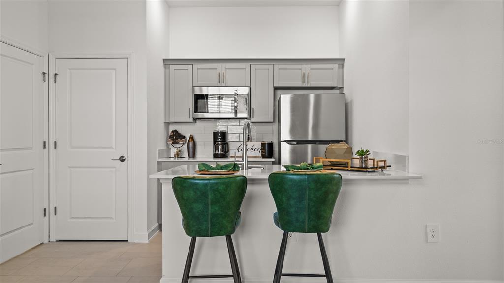 A small kitchen features gray cabinets, stainless steel appliances, and two green bar stools — 4103 EASTMINSTER ROAD, DAVENPORT, FL