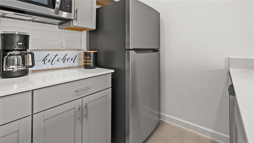 A kitchen features gray cabinets, white countertops, a stainless steel refrigerator, and a coffee maker — 4103 EASTMINSTER ROAD, DAVENPORT, FL