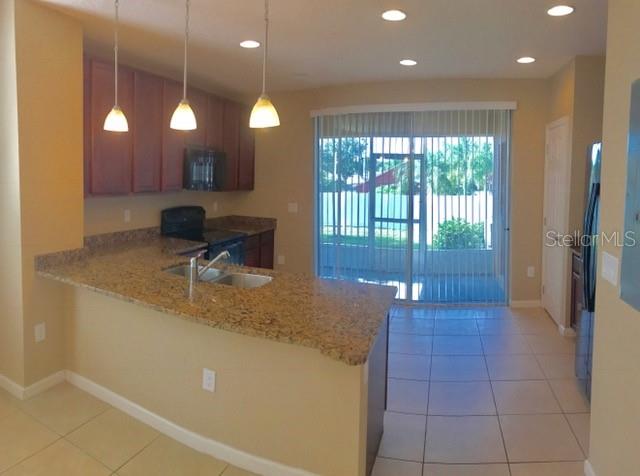 A kitchen with granite countertops, wooden cabinets, and pendant lighting overlooks a sliding glass door — 1102 CHELSEA DRIVE, DAVENPORT, FL