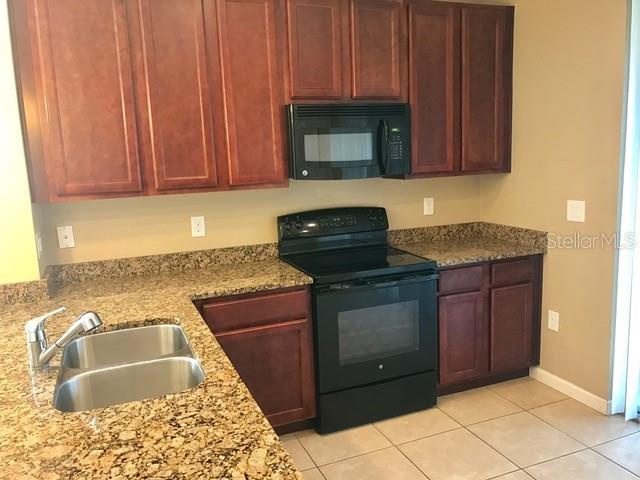 A kitchen features dark wood cabinets, granite countertops, and black appliances — 1102 CHELSEA DRIVE, DAVENPORT, FL