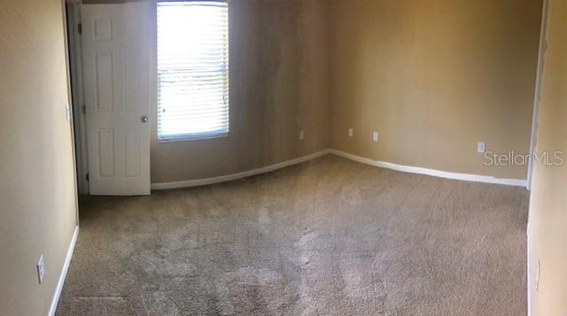 An empty bedroom features beige walls, tan carpeting, and a window with white blinds — 1102 CHELSEA DRIVE, DAVENPORT, FL