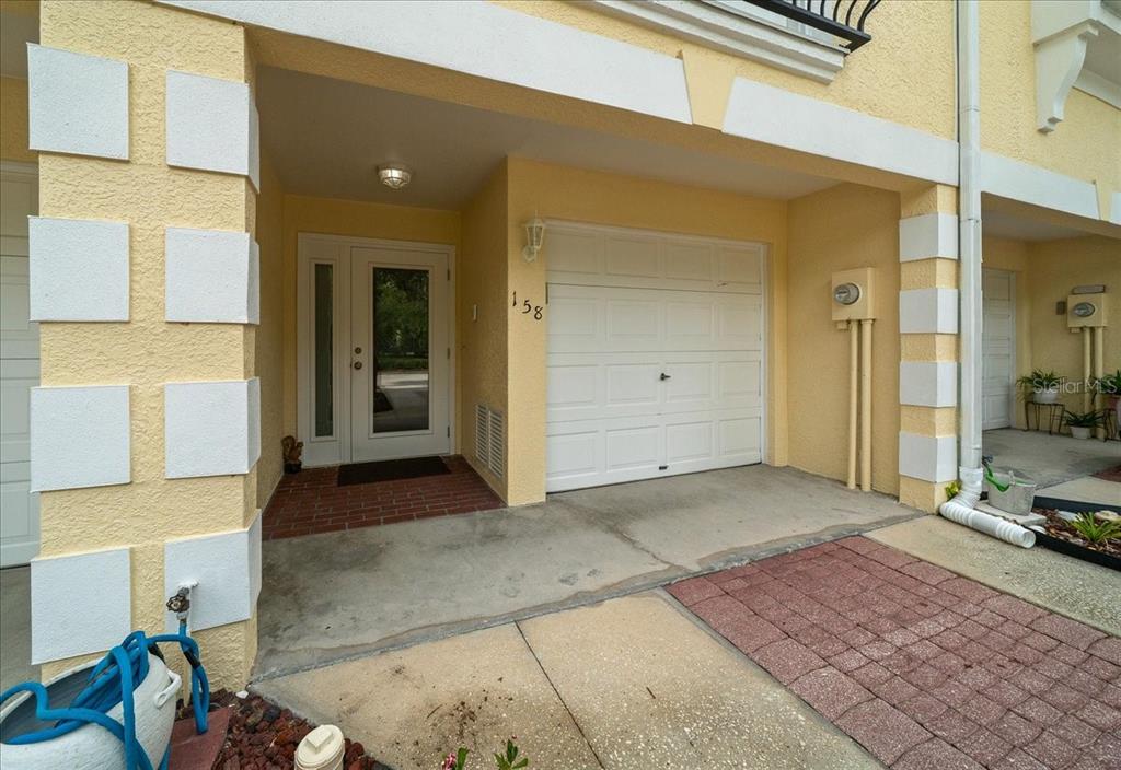 The exterior of a yellow townhouse features a white garage door and a front entrance — 158 BRENT CIRCLE, OLDSMAR, FL