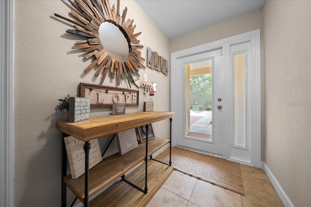 An entryway features a wooden console table, a sunburst mirror, and a glass-paneled front door — 158 BRENT CIRCLE, OLDSMAR, FL