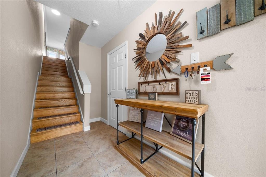 A foyer features a wooden console table, a sunburst mirror, and stairs leading to an upper level — 158 BRENT CIRCLE, OLDSMAR, FL