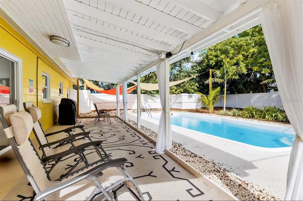 A covered patio with lounge chairs overlooks a swimming pool in a fenced backyard — 8215 QUAIL ROAD, SEMINOLE, FL