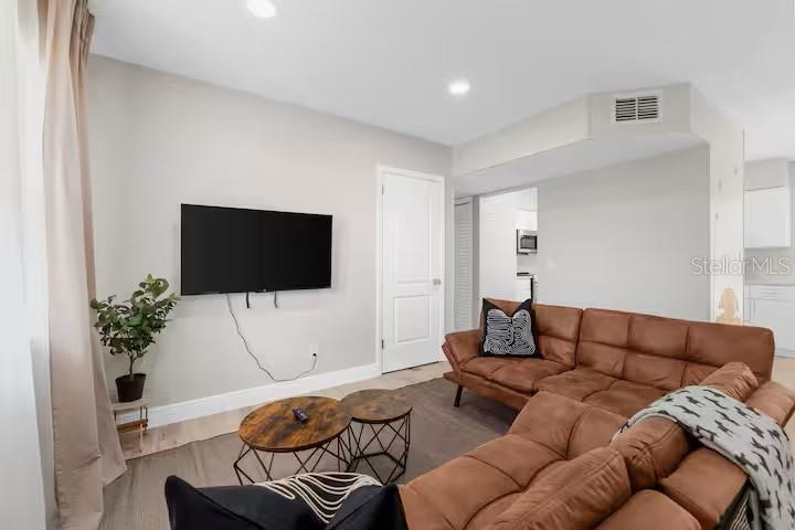 A living room features a brown sectional sofa, a wall-mounted television, and two round tables — 8215 QUAIL ROAD, SEMINOLE, FL