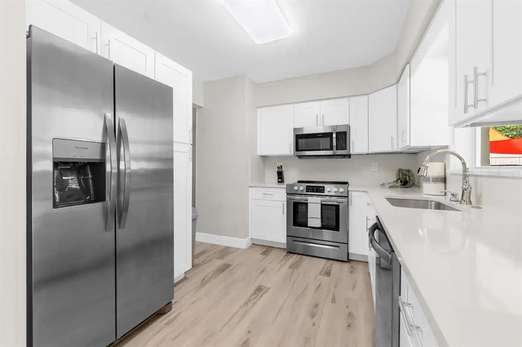 A modern kitchen features white cabinets, stainless steel appliances, and light wood-look flooring — 8215 QUAIL ROAD, SEMINOLE, FL