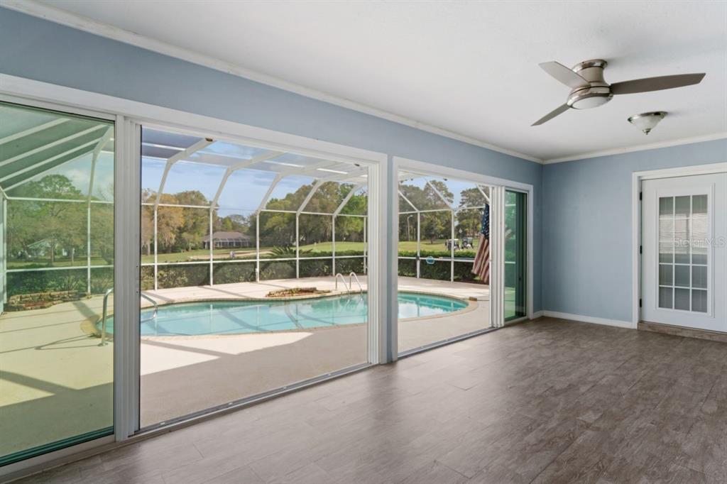 A sunroom with light blue walls, wood-look flooring, and sliding glass doors overlooking a pool — 375 E LIBERTY STREET, HERNANDO, FL