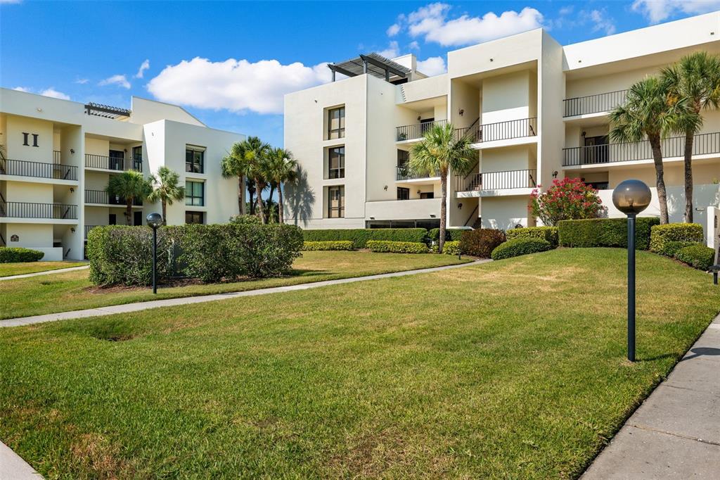 A grassy courtyard sits between two multi-story apartment buildings with balconies and palm trees — 50 COE ROAD UNIT 331, BELLEAIR, FL