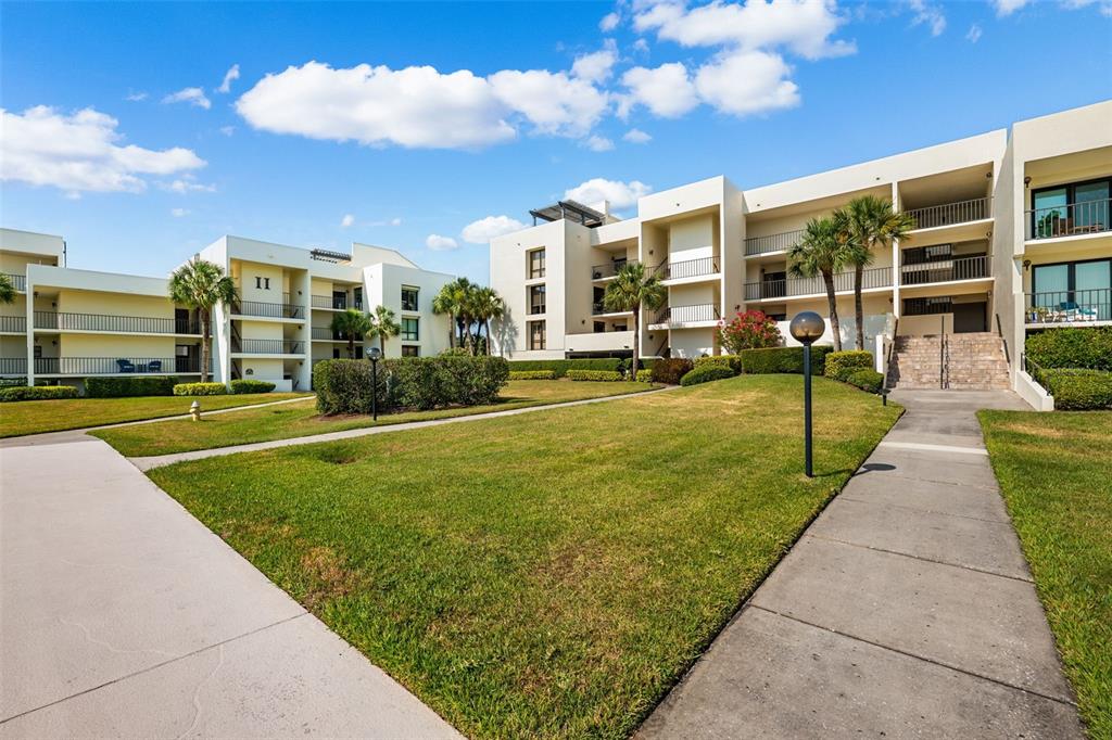 Exterior view of multi-story apartment buildings with balconies, a grassy lawn, and concrete walkways — 50 COE ROAD UNIT 331, BELLEAIR, FL