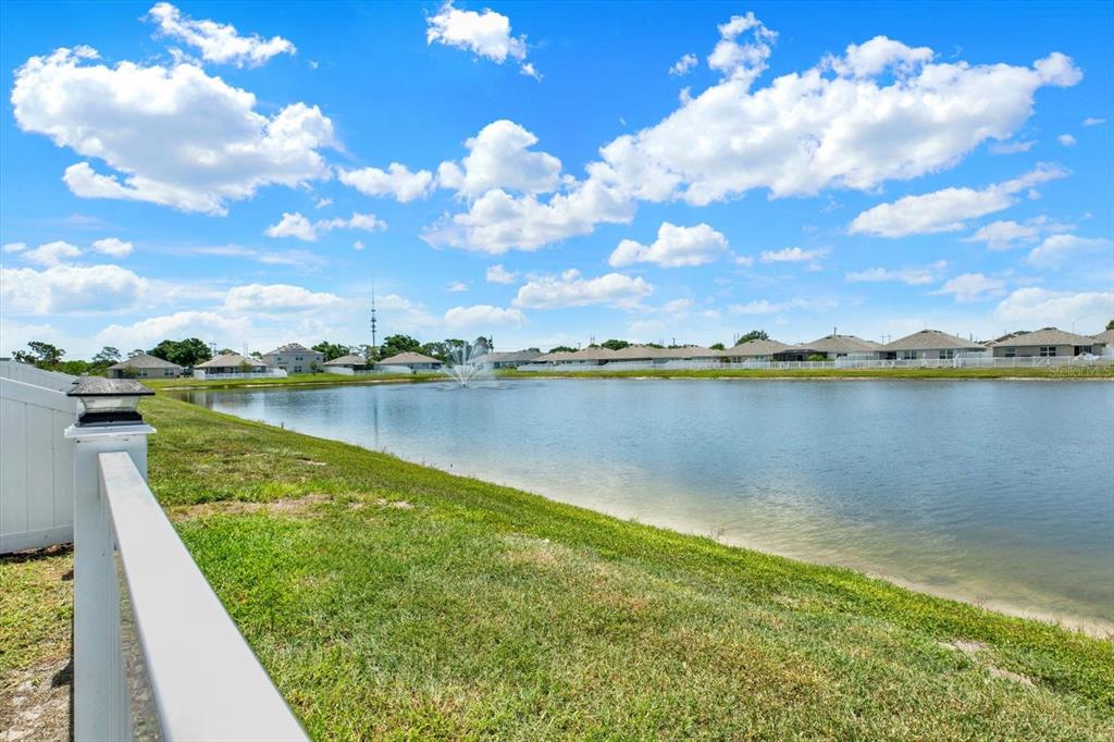 A view of a pond with a fountain behind a white fence and grassy yard — 1013 TIDAL ROCK AVE, RUSKIN, FL