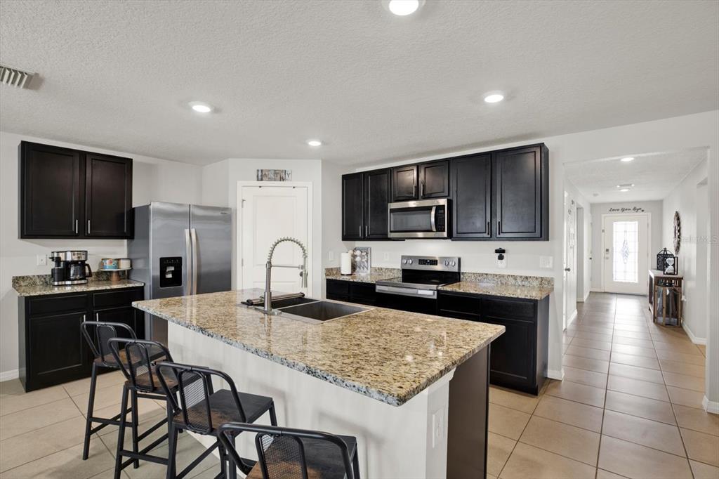 A living room with brown leather furniture, a circular metal shelf, and an open kitchen — 1013 TIDAL ROCK AVE, RUSKIN, FL