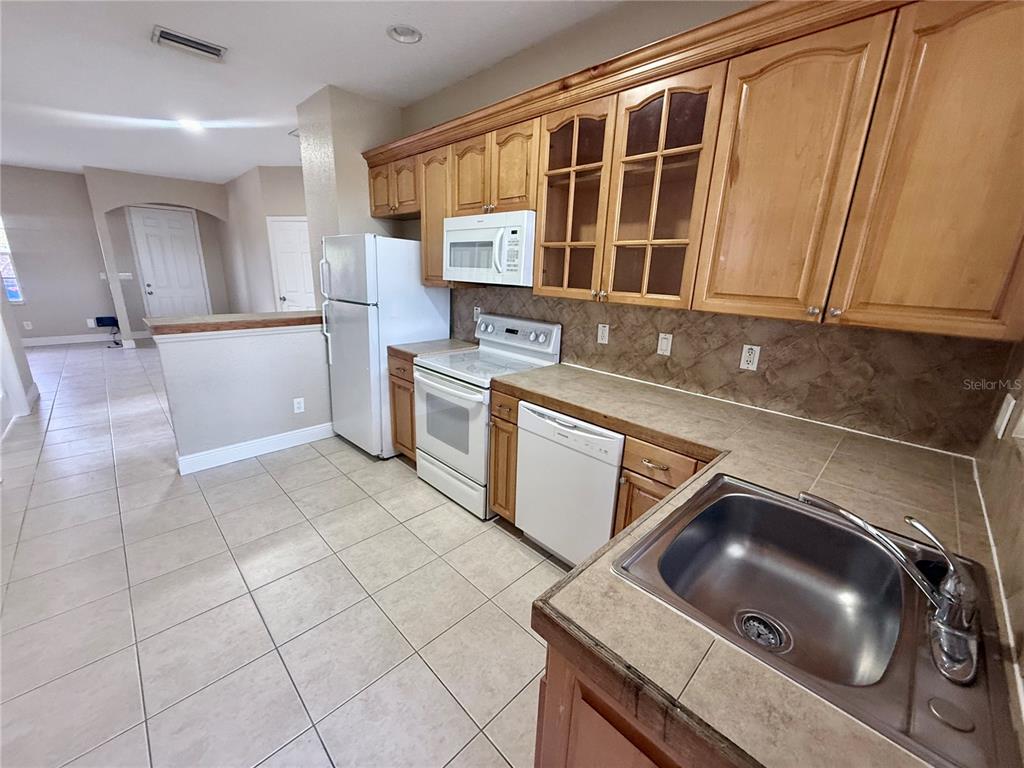 A kitchen features light wood cabinets, white appliances, tile countertops, and a tile floor — 9322 ANITA AVENUE, ENGLEWOOD, FL