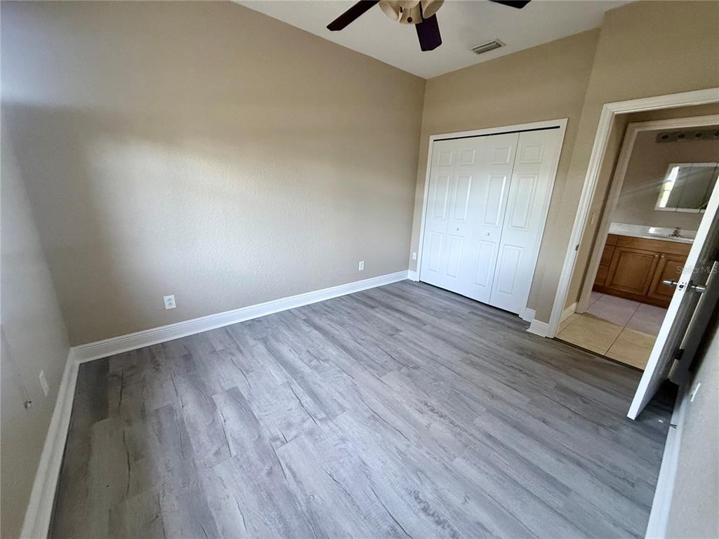 A bedroom with light-colored walls, gray wood-look flooring, a white closet, and an attached bathroom — 9322 ANITA AVENUE, ENGLEWOOD, FL