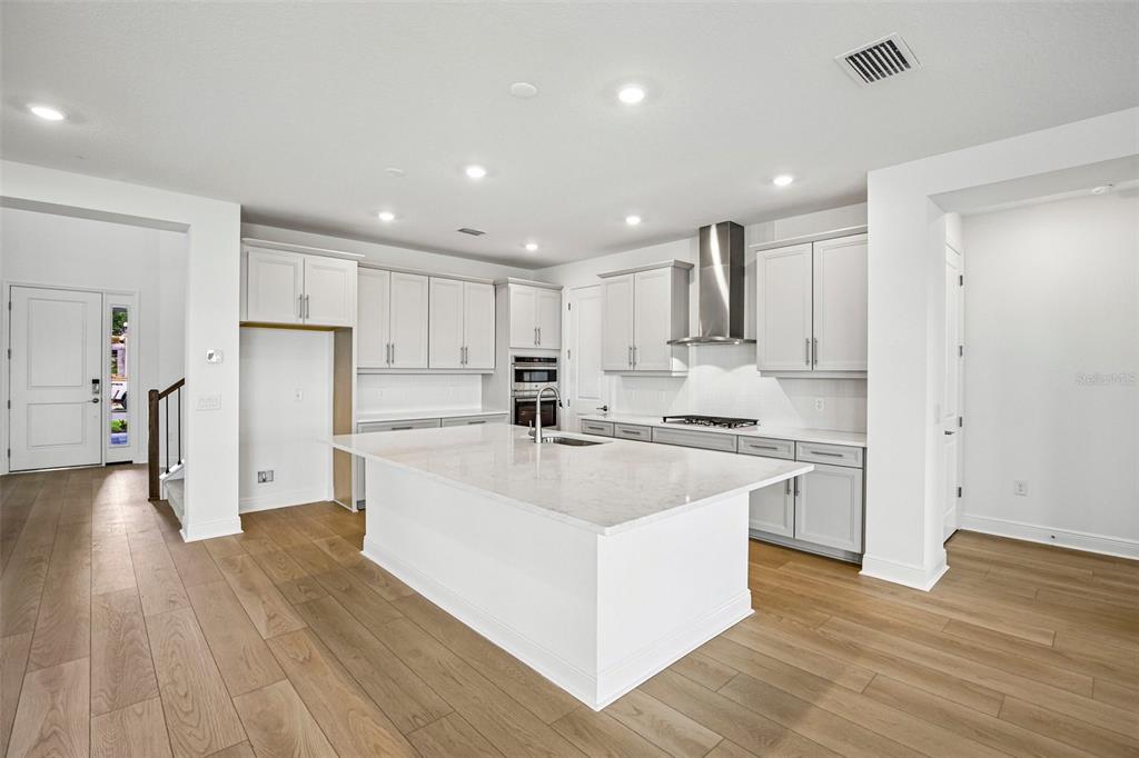 A modern kitchen features white cabinetry, a large central island, and light wood flooring — 7551 HAWKSTONE DRIVE, SARASOTA, FL