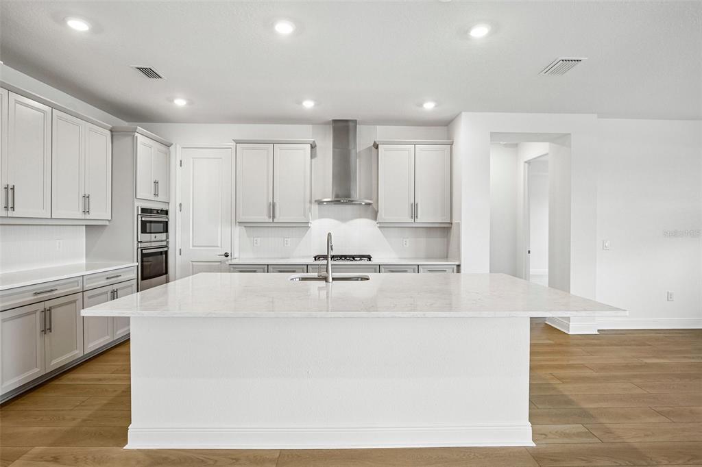 A modern kitchen features white cabinets, a large central island, and stainless steel appliances — 7551 HAWKSTONE DRIVE, SARASOTA, FL