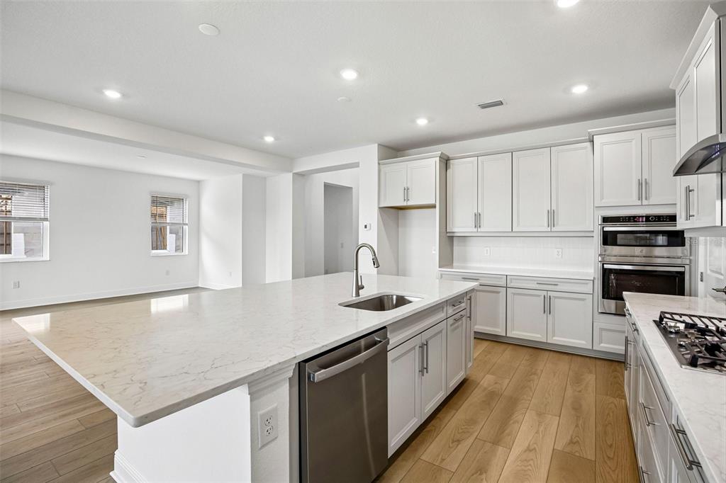 A modern kitchen features white cabinetry, a large marble-topped island, and light wood flooring — 7551 HAWKSTONE DRIVE, SARASOTA, FL