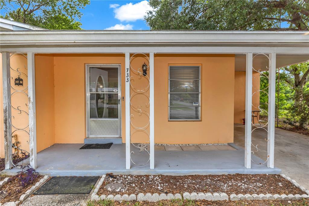 The exterior of a peach-colored house features a covered porch with decorative white metal columns — 733 HAGER STREET, DELTONA, FL