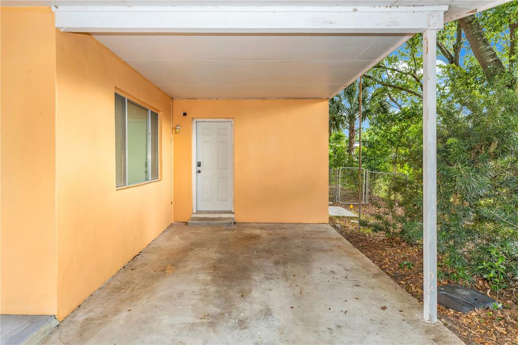 A covered concrete carport features an orange exterior wall, a white door, and a window — 733 HAGER STREET, DELTONA, FL