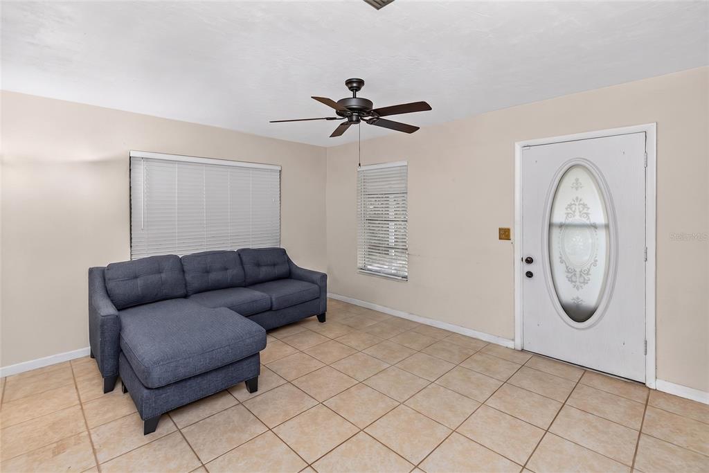 A living room features a blue sectional sofa, tile flooring, a ceiling fan, and a door — 733 HAGER STREET, DELTONA, FL