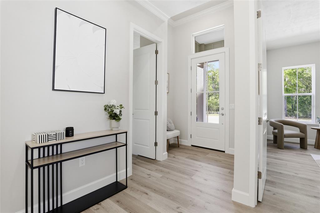 A bright entryway features light wood flooring, a modern console table, and a glass-paneled front door — 13425 SW 9TH ROAD, NEWBERRY, FL