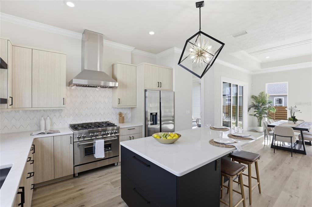 A modern kitchen features light wood cabinets, a dark island, stainless steel appliances, and pendant lighting — 13425 SW 9TH ROAD, NEWBERRY, FL