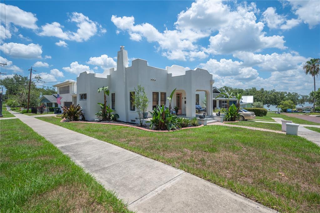 A white stucco house with a mission-style roofline sits on a corner lot with landscaping — 1102 MELTON AVENUE, LAKELAND, FL