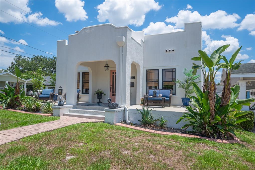 A white stucco bungalow features a covered front porch, a pink door, and landscaping — 1102 MELTON AVENUE, LAKELAND, FL
