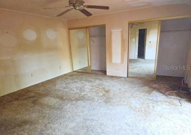 A bedroom with beige walls, a ceiling fan, mirrored closet doors, and worn carpeting — 188 MOONSTONE COURT, PORT ORANGE, FL