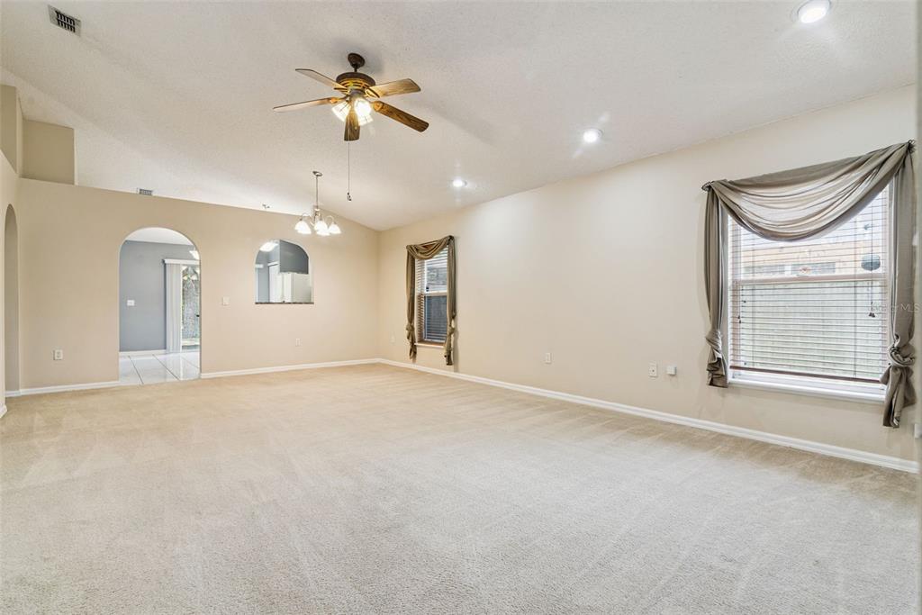 A spacious, carpeted living room features a vaulted ceiling, a ceiling fan, and two windows — 3308 ERSKINE DRIVE, ORLANDO, FL
