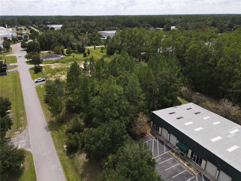 An aerial view shows a paved road, a wooded lot, and a commercial warehouse building — LOT 4 & LOT 5 NW 16TH STREET, GAINESVILLE, FL