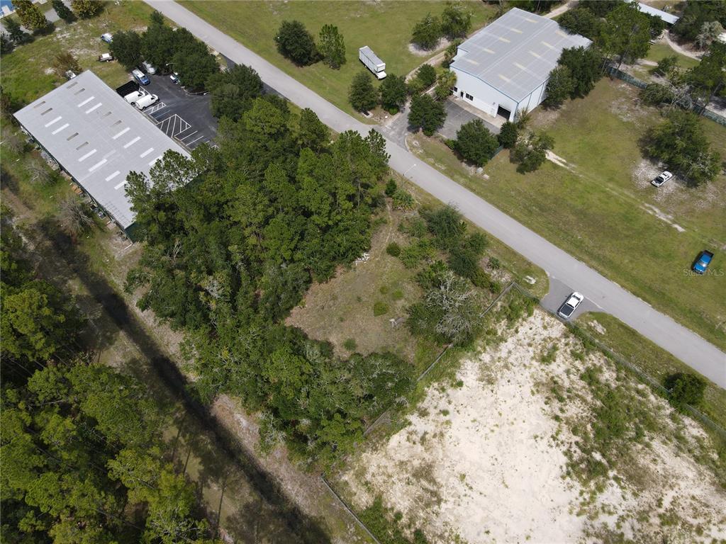 An aerial view shows a vacant, partially wooded lot situated between two commercial warehouse buildings — LOT 4 & LOT 5 NW 16TH STREET, GAINESVILLE, FL