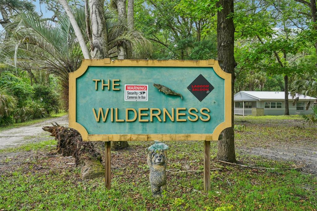 A sign reading The Wilderness stands in a wooded area near a small house — 217 S TUCK POINT, INVERNESS, FL