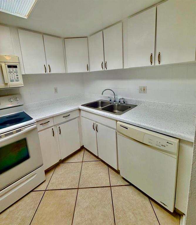 A kitchen features white cabinets, white appliances, a double-basin sink, and light-colored tiled flooring — 20 SHEOAH BOULEVARD UNIT 9, WINTER SPRINGS, FL