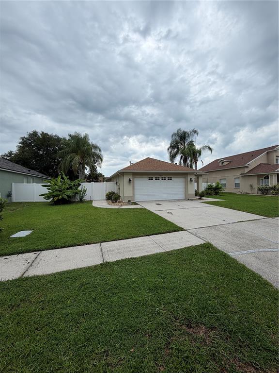 A single-story house with a white garage door, tan siding, and a white privacy fence — 24312 SILKBAY COURT, LUTZ, FL
