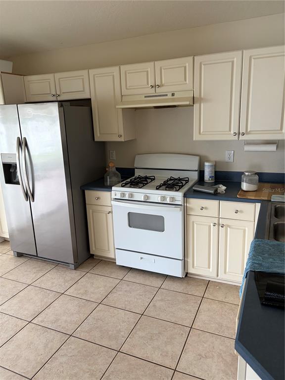A kitchen features white cabinets, a stainless steel refrigerator, a white gas stove, and tiled floors — 24312 SILKBAY COURT, LUTZ, FL