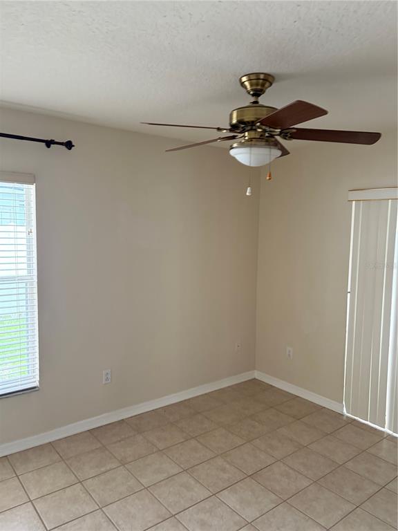 An empty room with beige walls, tile flooring, a ceiling fan, and vertical blinds — 24312 SILKBAY COURT, LUTZ, FL