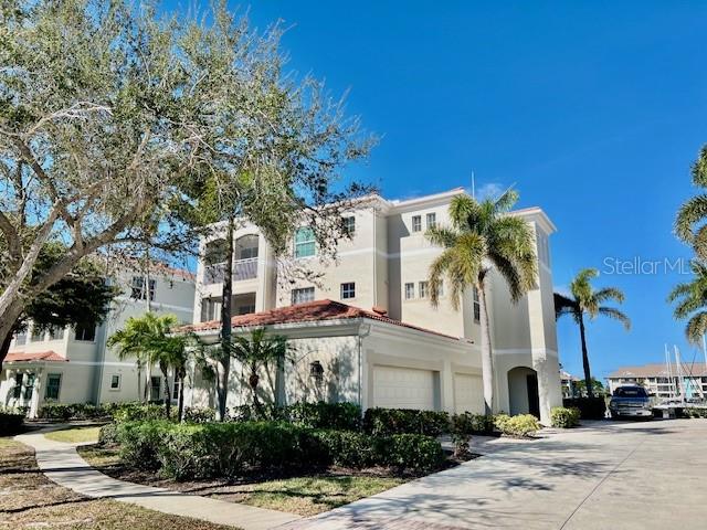 A multi-story residential building with a tan facade, palm trees, and a paved driveway — 3471 SUNSET KEY CIRCLE UNIT 102, PUNTA GORDA, FL