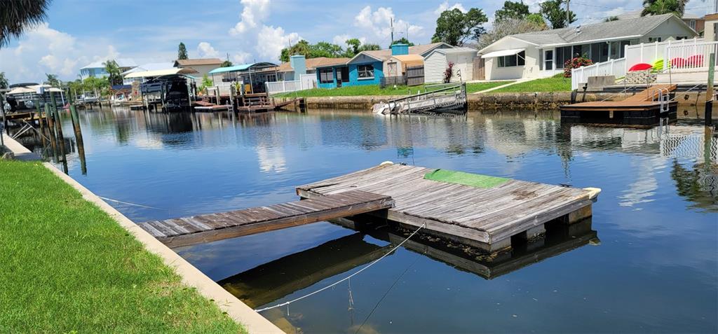A wooden floating dock sits in a residential canal lined with houses and boat slips — 13240 STARFISH DRIVE, HUDSON, FL