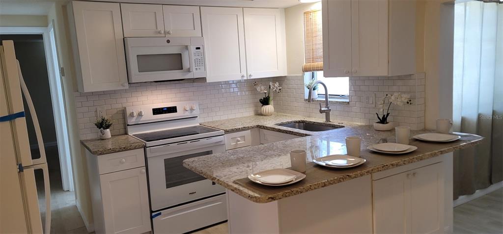 A kitchen features white cabinets, granite countertops, a white stove, and a subway tile backsplash — 13240 STARFISH DRIVE, HUDSON, FL