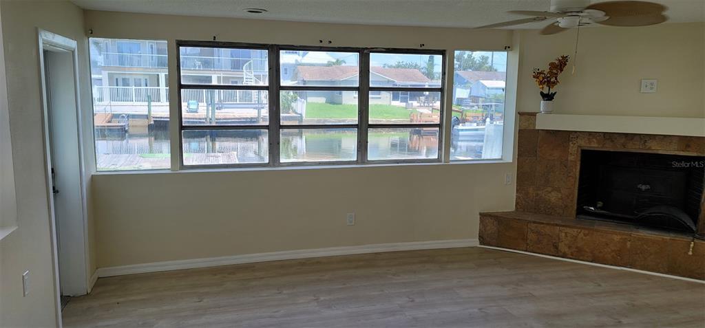 A living room features light wood-look flooring, a tiled fireplace, and large windows overlooking water — 13240 STARFISH DRIVE, HUDSON, FL