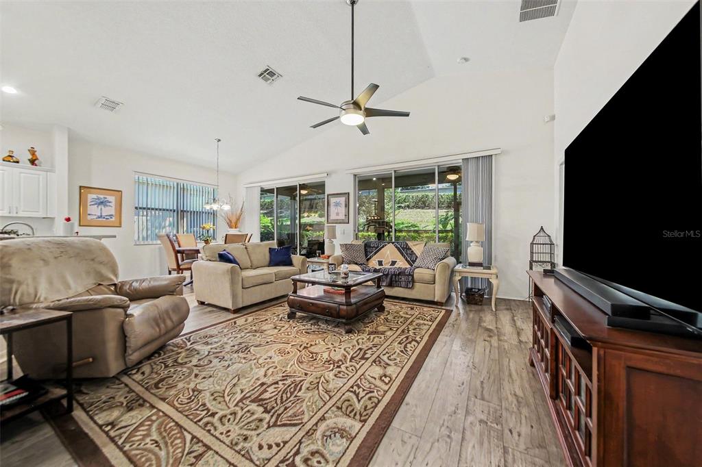 A living room with wood-look flooring, a ceiling fan, and an open kitchen in back — 2361 PRAIRIE DUNES, CLERMONT, FL