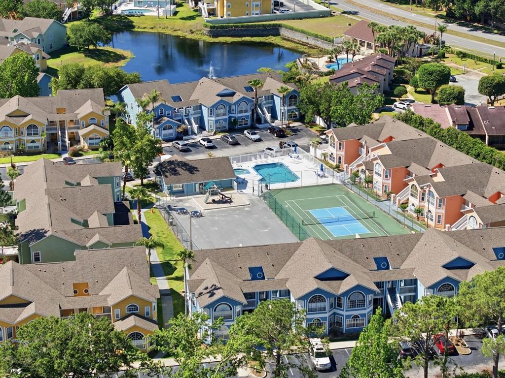An aerial view of an apartment complex featuring a swimming pool, tennis court, and pond — 3153 BRITANNIA BOULEVARD UNIT B, KISSIMMEE, FL