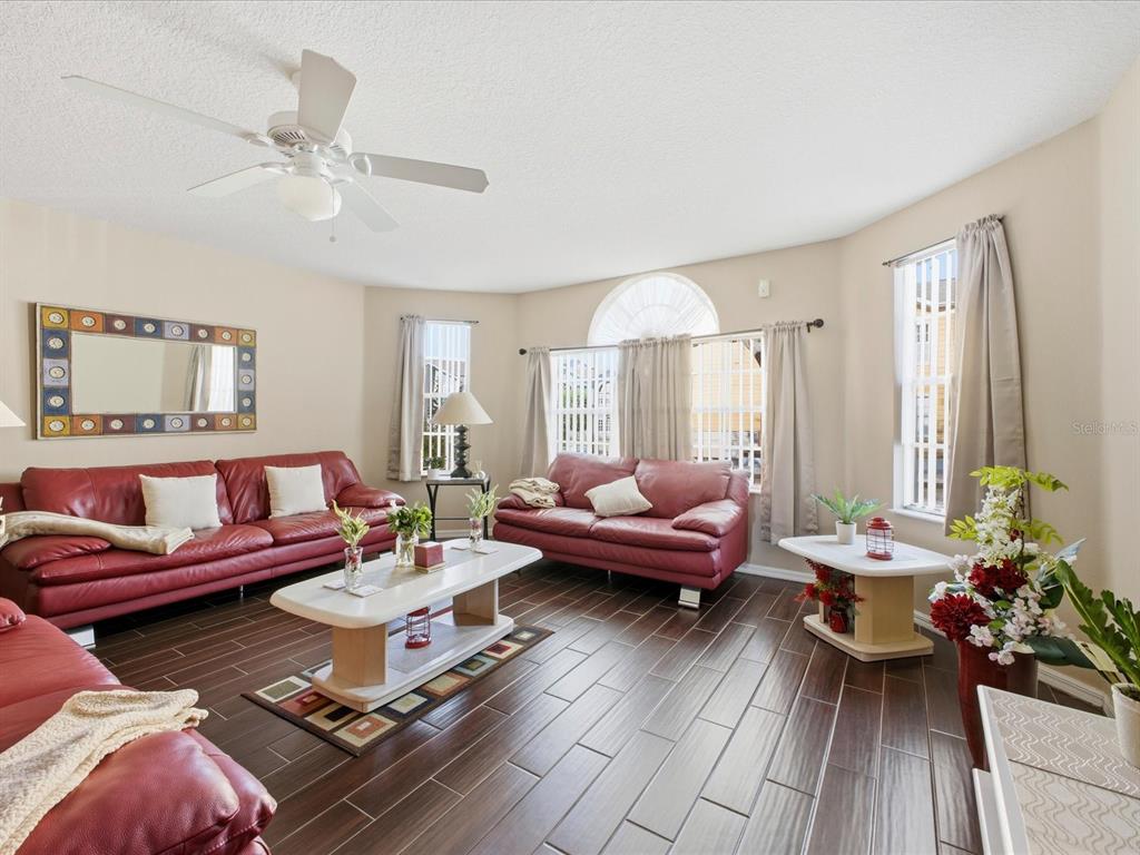 A living room features red leather sofas, dark wood-look tile flooring, and a ceiling fan — 3153 BRITANNIA BOULEVARD UNIT B, KISSIMMEE, FL