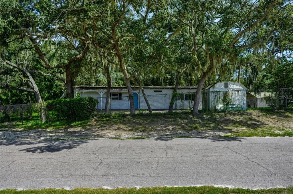 A single-story mobile home with a blue door sits behind a chain-link fence under trees — 12489 SW 45TH TERRACE, WEBSTER, FL