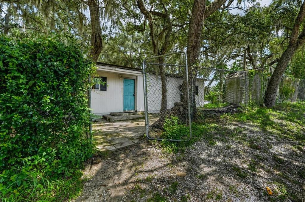 A white house with a blue door sits behind a chain-link fence under large trees — 12489 SW 45TH TERRACE, WEBSTER, FL